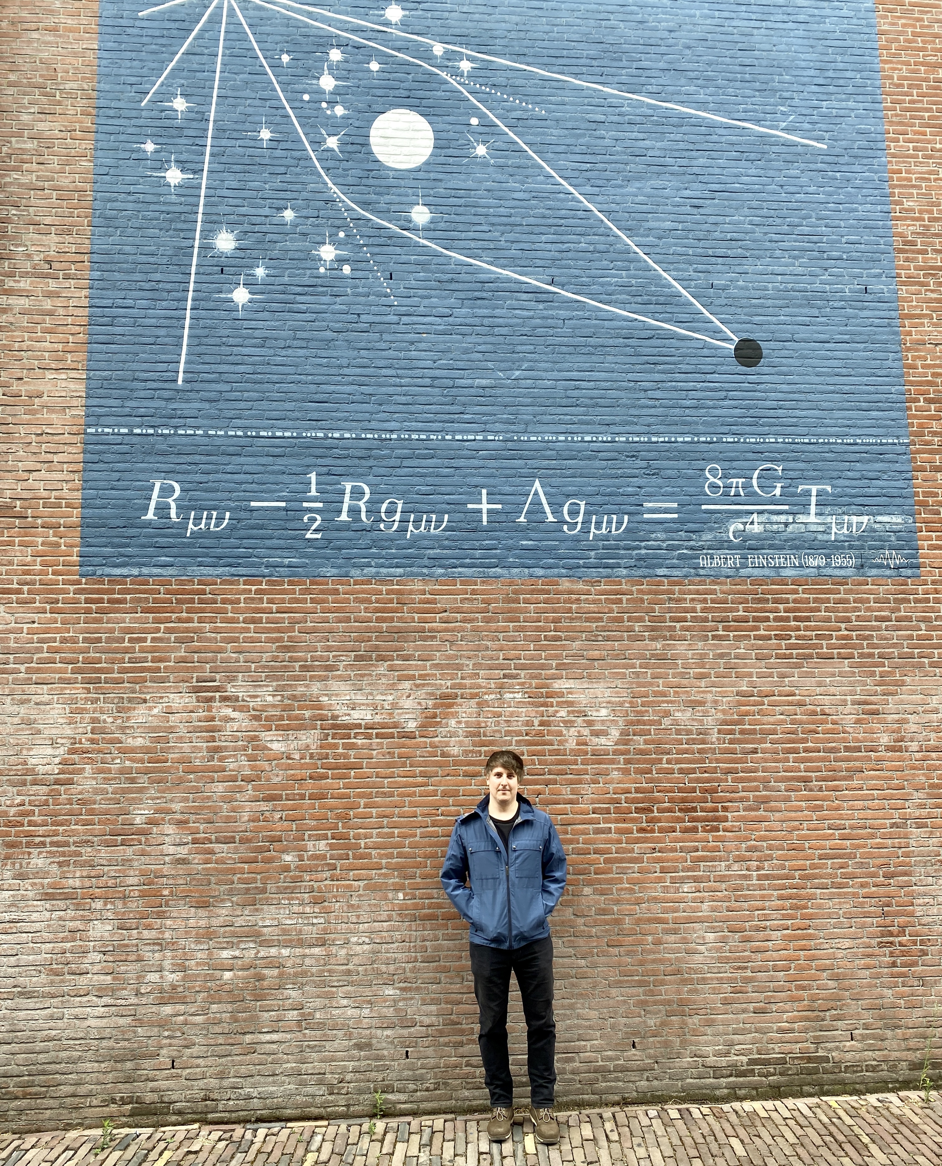 Sebastian Murk standing in front of the Einstein field equations mural in Leiden.